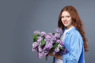 Photo of Smiling teenage girl with bouquet of lilac flowers on grey background. Space for text