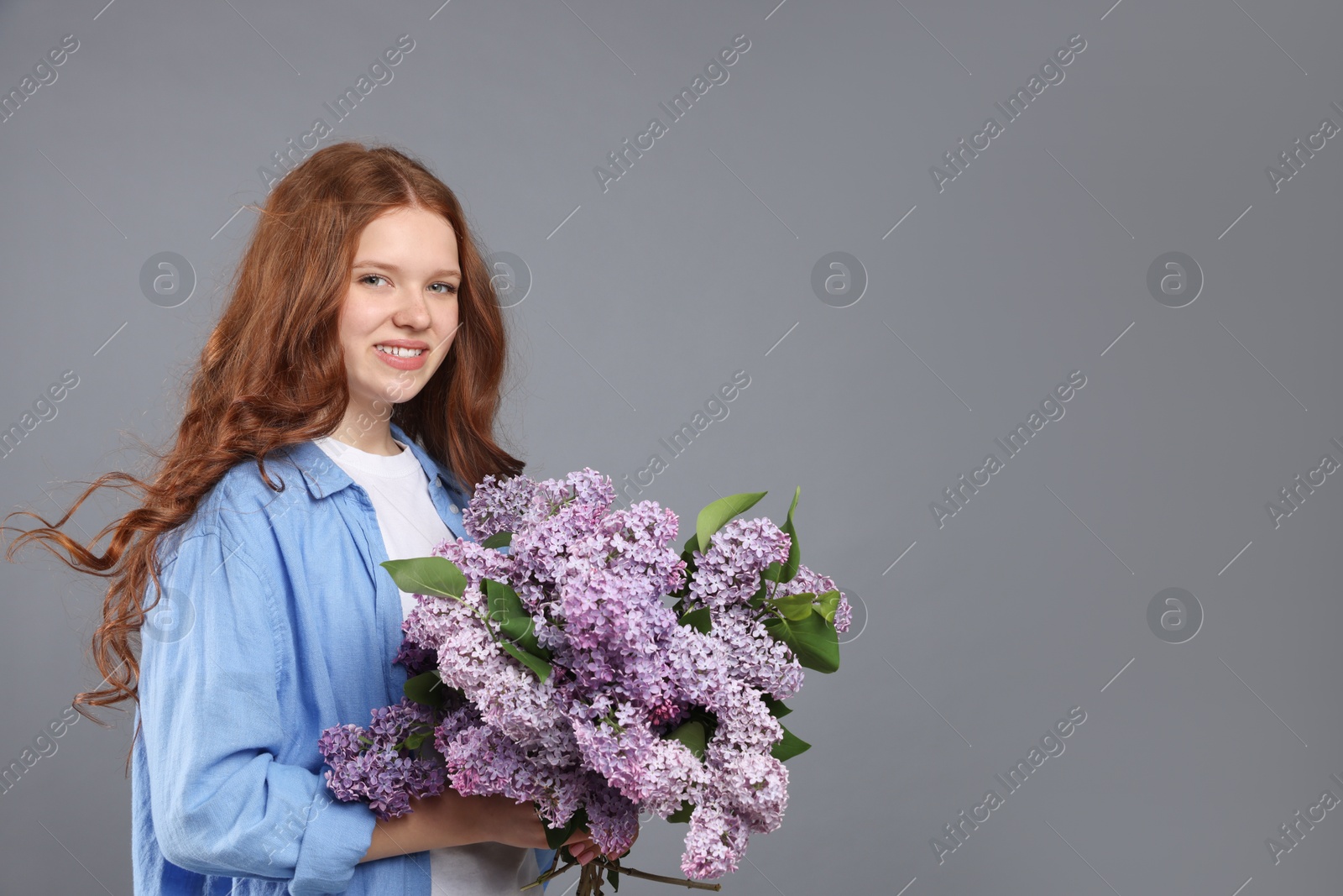 Smiling teenage girl with bouquet of lilac flowers on grey background. Space for text Photo of Smiling teenage girl with bouquet of lilac flowers on grey background. Space for text