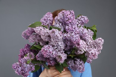 Photo of Teenage girl hiding behind bouquet of lilac flowers on grey background