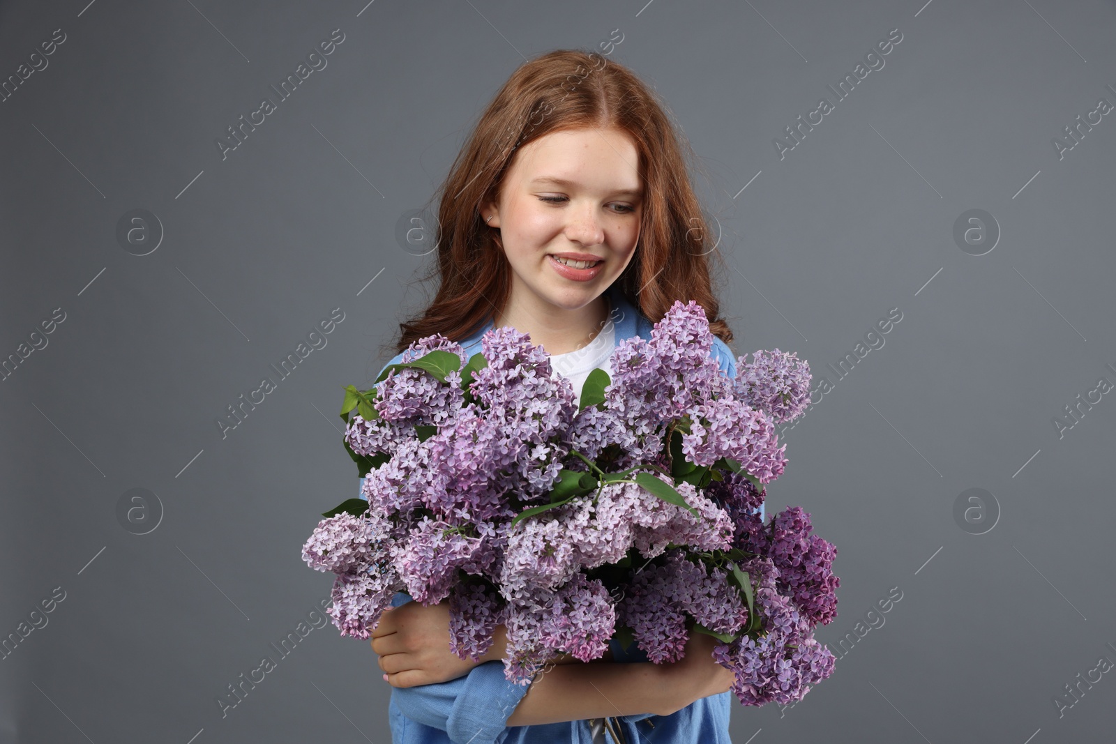 Portrait of smiling teenage girl with lilac flowers on grey background Photo of Portrait of smiling teenage girl with lilac flowers on grey background