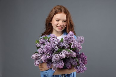 Photo of Portrait of smiling teenage girl with lilac flowers on grey background