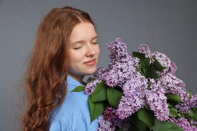 Photo of Portrait of beautiful teenage girl with lilac flowers on grey background