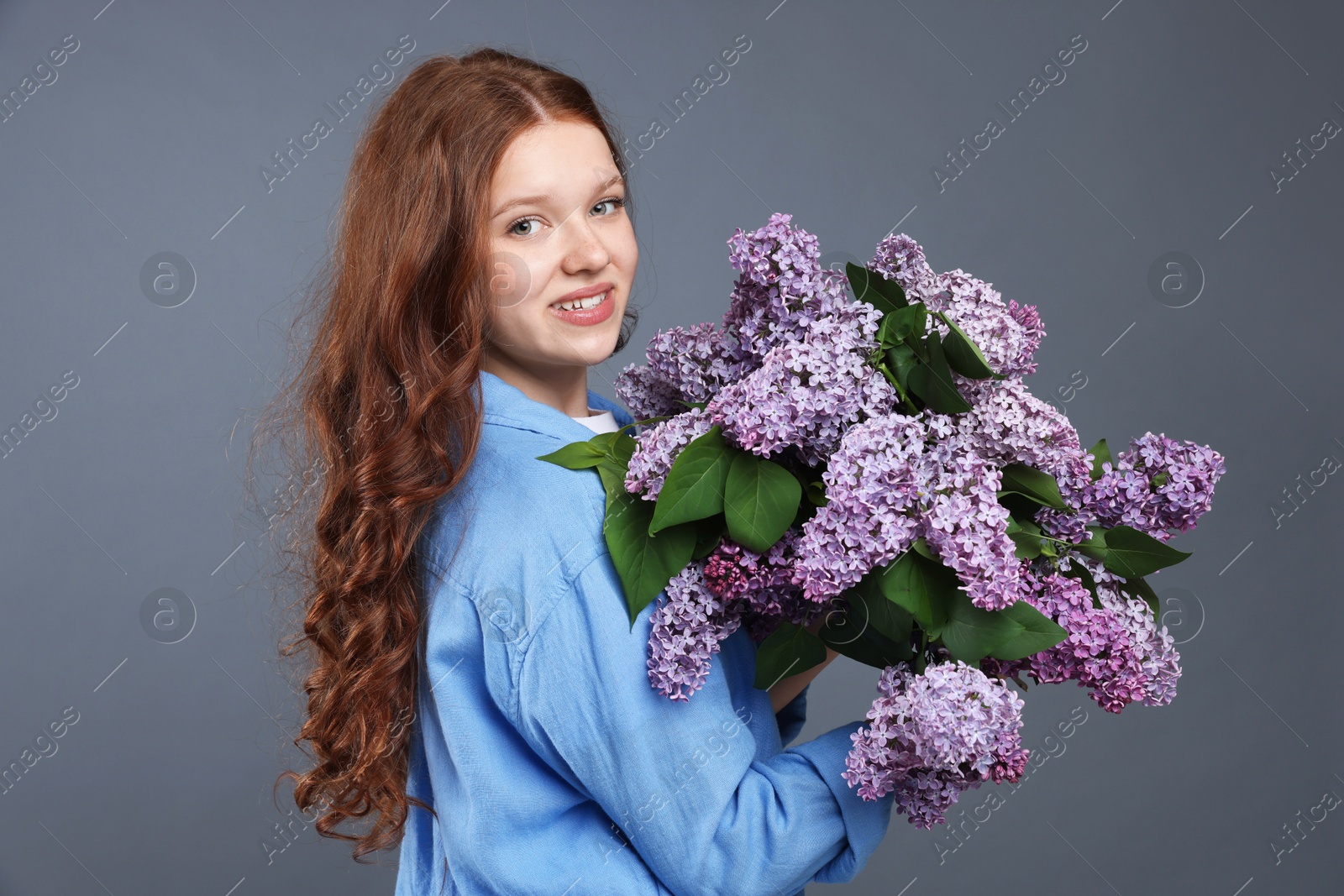 Portrait of smiling teenage girl with lilac flowers on grey background Photo of Portrait of smiling teenage girl with lilac flowers on grey background