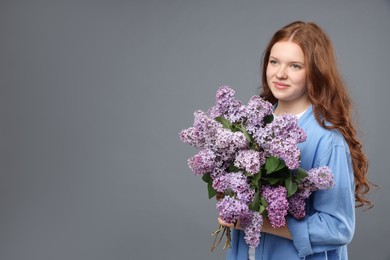 Photo of Beautiful teenage girl with bouquet of lilac flowers on grey background. Space for text