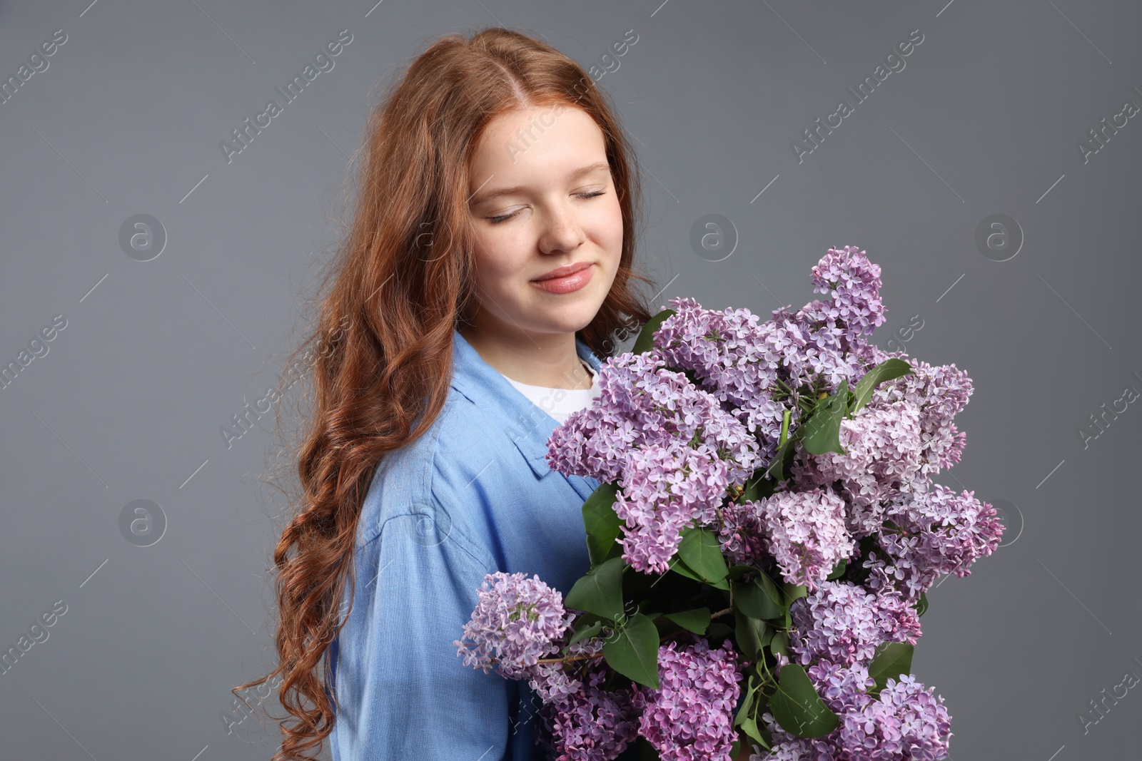 Portrait of beautiful teenage girl with lilac flowers on grey background Photo of Portrait of beautiful teenage girl with lilac flowers on grey background