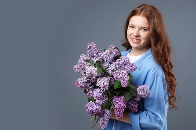 Photo of Smiling teenage girl with bouquet of lilac flowers on grey background. Space for text