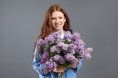 Photo of Portrait of smiling teenage girl with lilac flowers on grey background