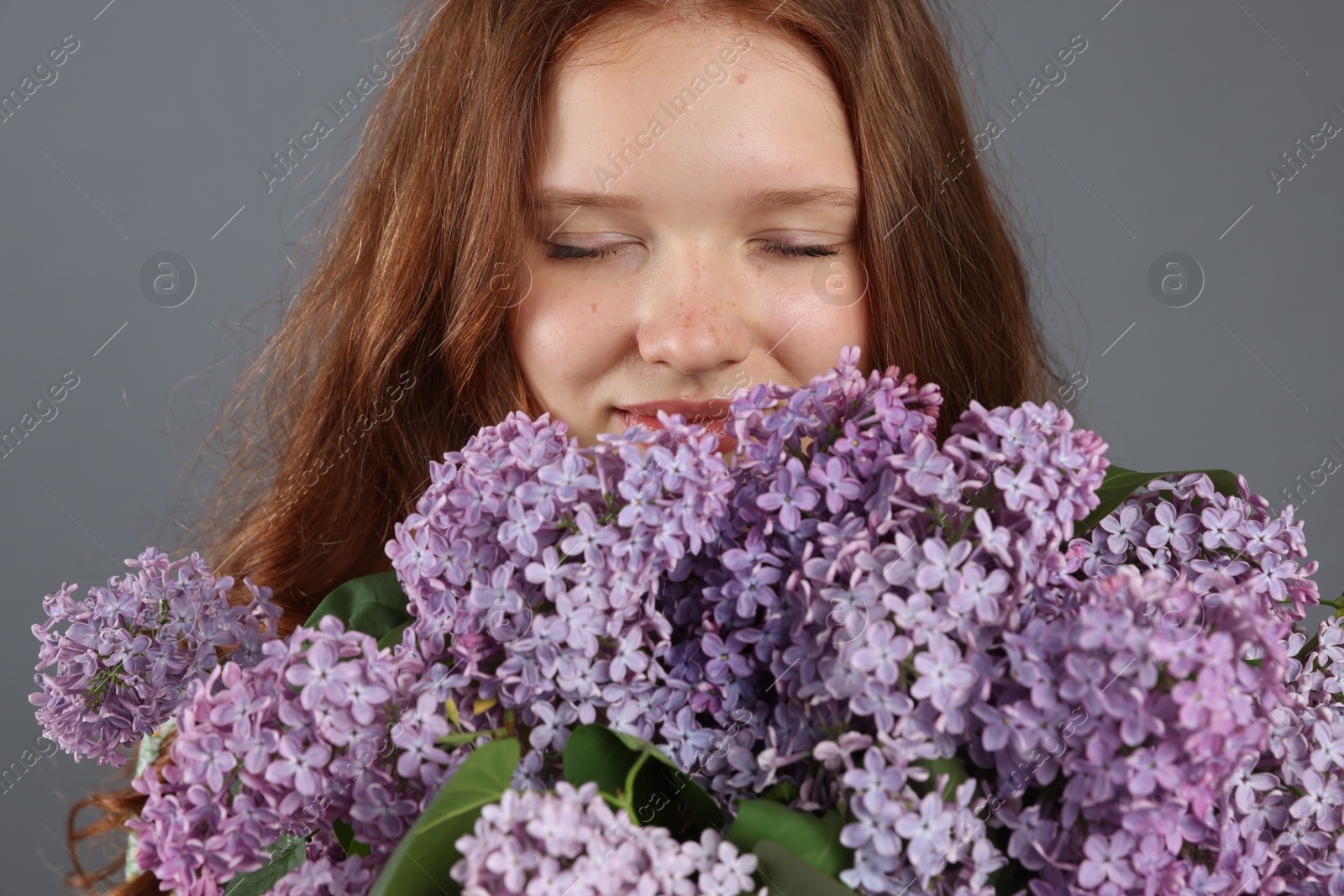 Beautiful teenage girl with bouquet of lilac flowers on grey background Photo of Beautiful teenage girl with bouquet of lilac flowers on grey background