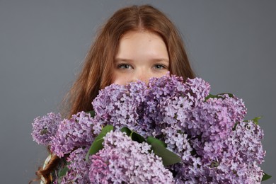Photo of Beautiful teenage girl with bouquet of lilac flowers on grey background