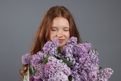 Photo of Beautiful teenage girl with bouquet of lilac flowers on grey background
