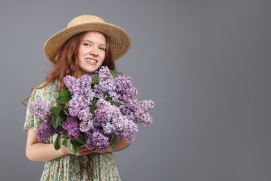 Photo of Smiling teenage girl with bouquet of lilac flowers on grey background. Space for text