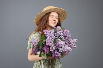 Photo of Smiling teenage girl with bouquet of lilac flowers on grey background
