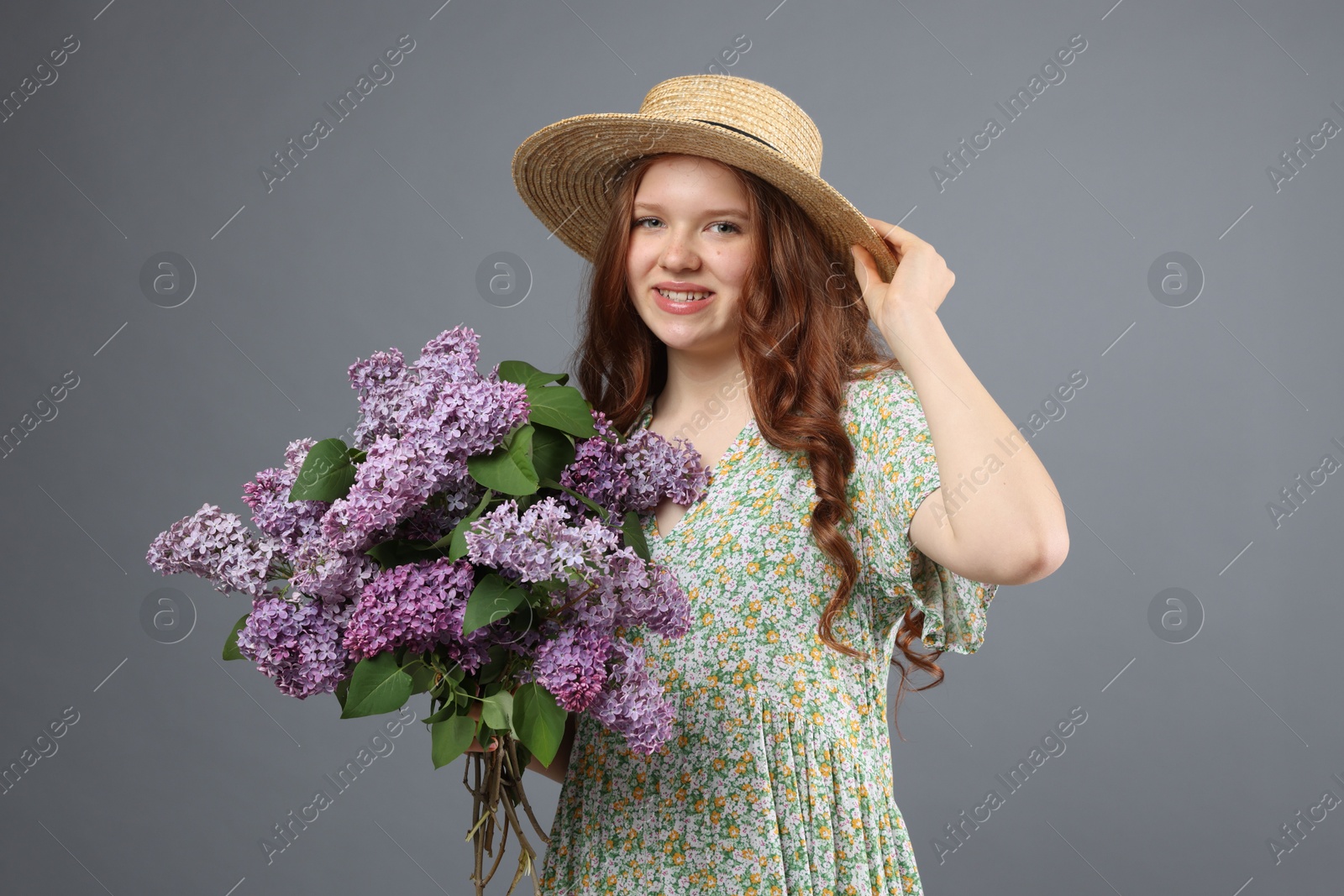 Portrait of smiling teenage girl with lilac flowers on grey background Photo of Portrait of smiling teenage girl with lilac flowers on grey background