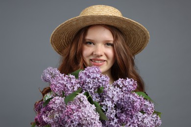 Photo of Portrait of smiling teenage girl with lilac flowers on grey background