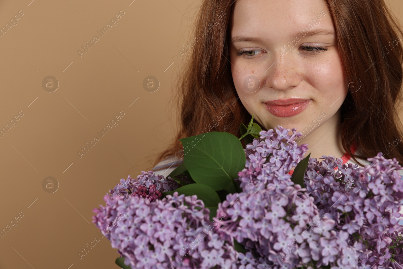 Beautiful teenage girl with bouquet of lilac flowers on beige background, closeup. Space for text Photo of Beautiful teenage girl with bouquet of lilac flowers on beige background, closeup. Space for text