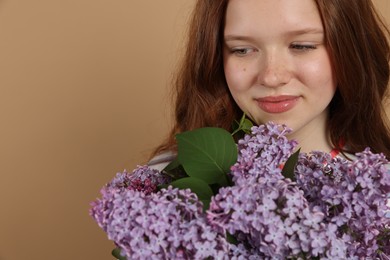 Photo of Beautiful teenage girl with bouquet of lilac flowers on beige background, closeup. Space for text