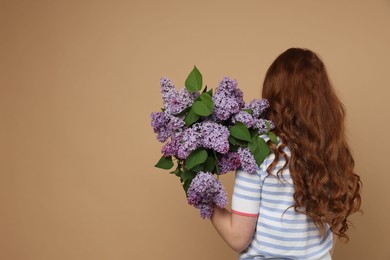 Photo of Teenage girl with bouquet of lilac flowers on beige background, back view. Space for text