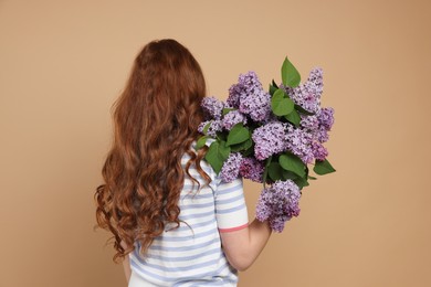 Photo of Teenage girl with bouquet of lilac flowers on beige background, back view