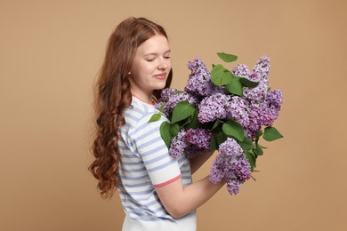 Photo of Beautiful teenage girl with bouquet of lilac flowers on beige background