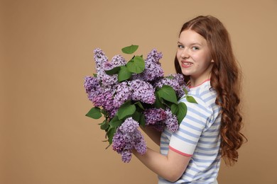 Photo of Smiling teenage girl with bouquet of lilac flowers on beige background. Space for text