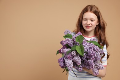 Photo of Beautiful teenage girl with bouquet of lilac flowers on beige background. Space for text