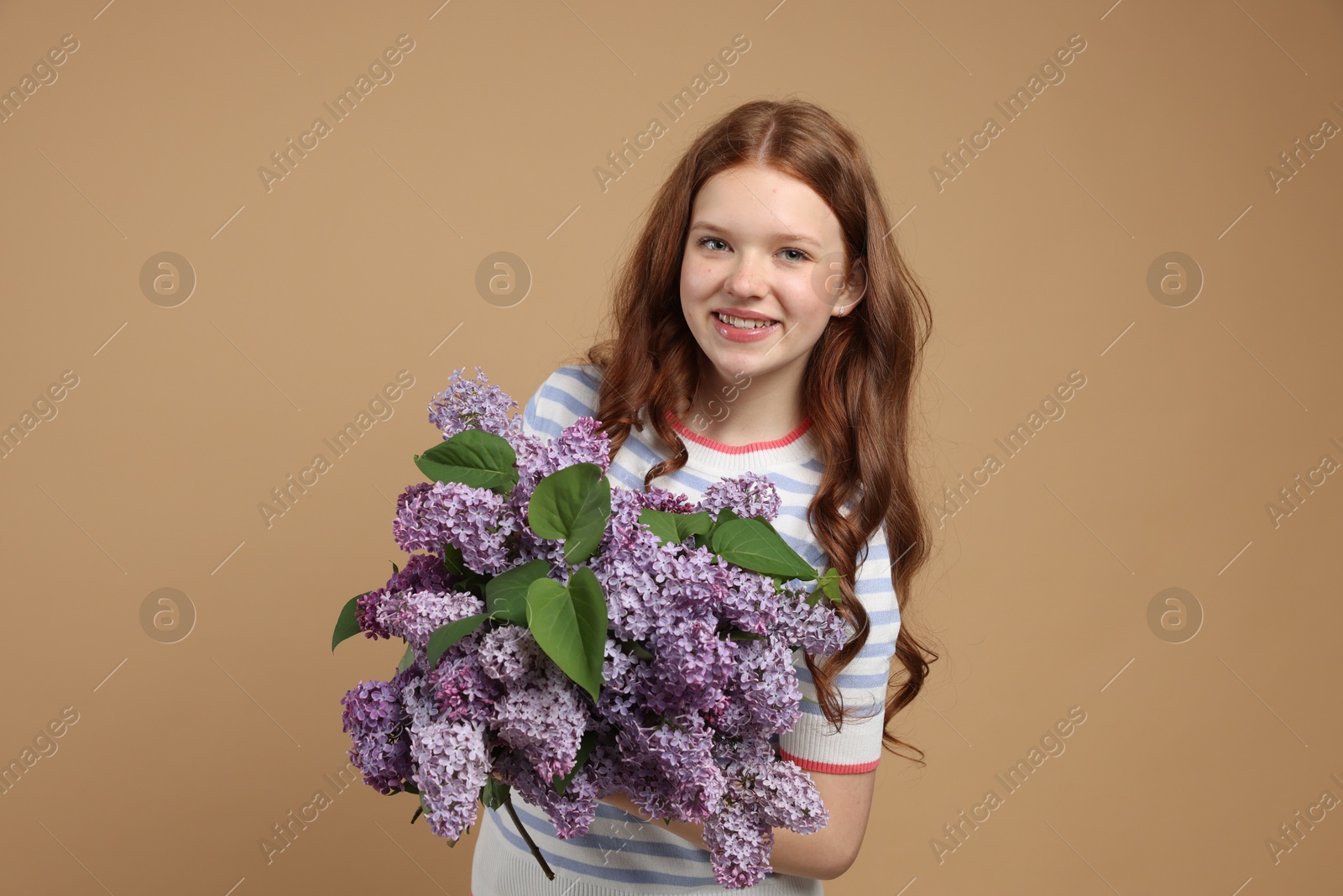 Smiling teenage girl with bouquet of lilac flowers on beige background Photo of Smiling teenage girl with bouquet of lilac flowers on beige background