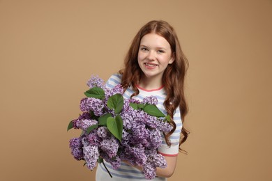 Photo of Smiling teenage girl with bouquet of lilac flowers on beige background