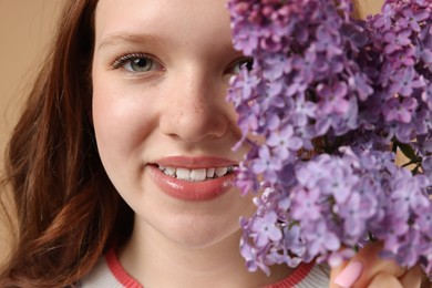 Photo of Smiling teenage girl with lilac flowers on beige background, closeup