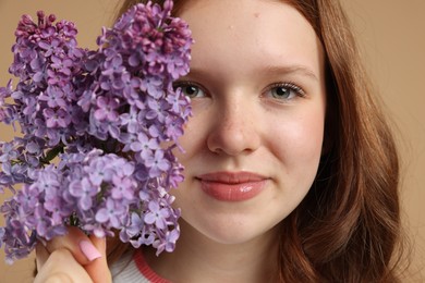 Photo of Beautiful teenage girl with lilac flowers on beige background, closeup