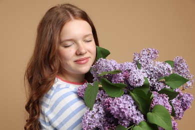 Photo of Beautiful teenage girl with bouquet of lilac flowers on beige background