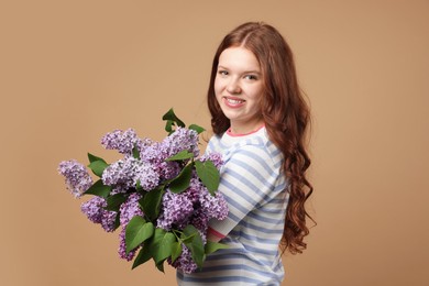 Photo of Smiling teenage girl with bouquet of lilac flowers on beige background