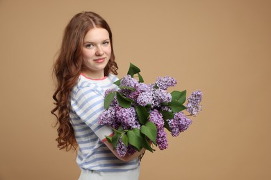 Photo of Beautiful teenage girl with bouquet of lilac flowers on beige background