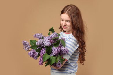 Photo of Beautiful teenage girl with bouquet of lilac flowers on beige background