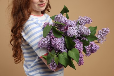 Photo of Teenage girl with bouquet of lilac flowers on beige background, closeup