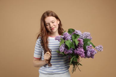 Photo of Beautiful teenage girl with bouquet of lilac flowers on beige background