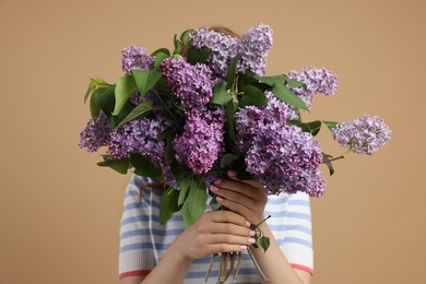 Photo of Teenage girl hiding behind bouquet of lilac flowers on beige background