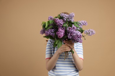 Photo of Teenage girl hiding behind bouquet of lilac flowers on beige background