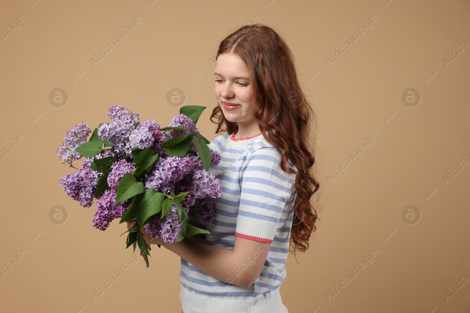 Beautiful teenage girl with bouquet of lilac flowers on beige background Photo of Beautiful teenage girl with bouquet of lilac flowers on beige background