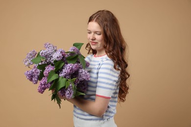 Photo of Beautiful teenage girl with bouquet of lilac flowers on beige background