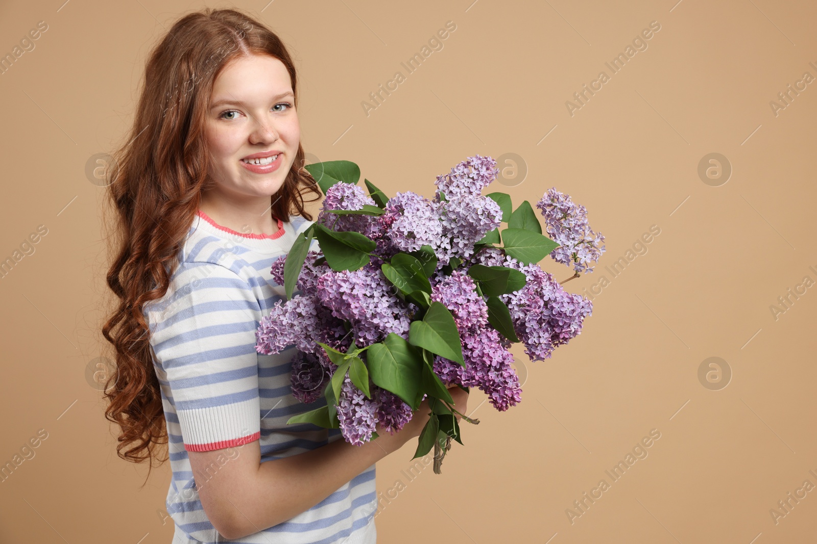 Smiling teenage girl with bouquet of lilac flowers on beige background Photo of Smiling teenage girl with bouquet of lilac flowers on beige background