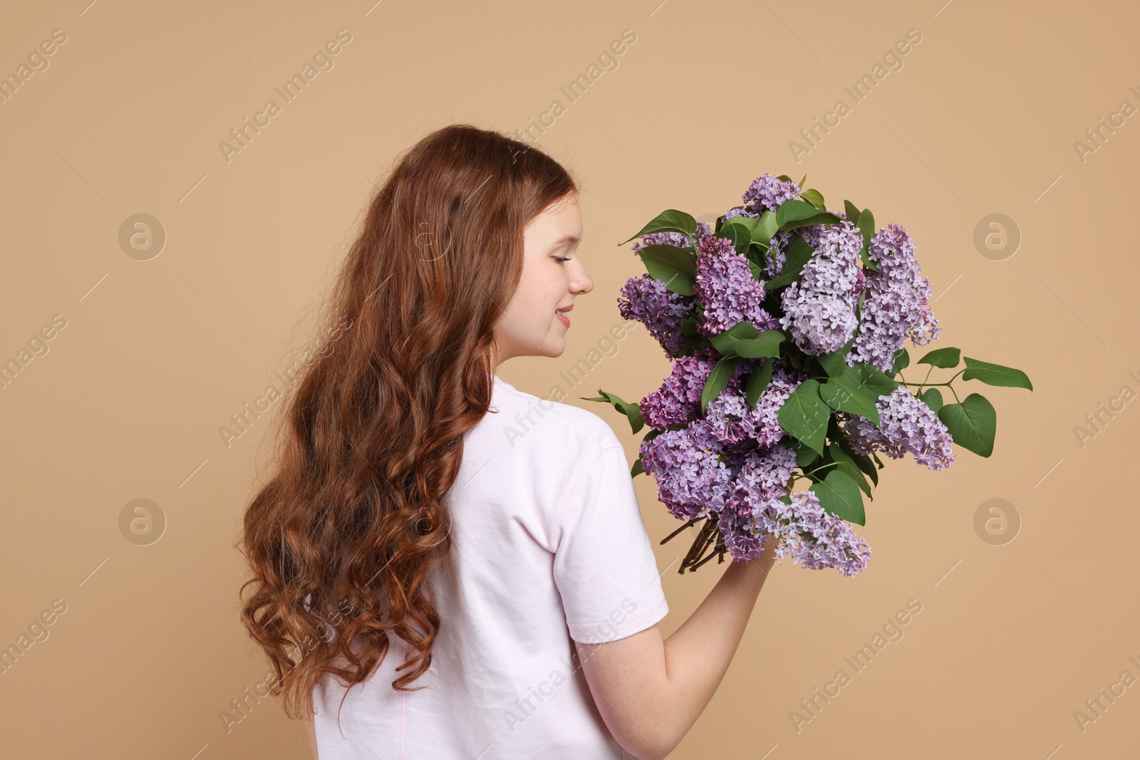 Teenage girl with bouquet of lilac flowers on beige background Photo of Teenage girl with bouquet of lilac flowers on beige background