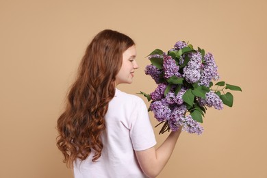 Photo of Teenage girl with bouquet of lilac flowers on beige background