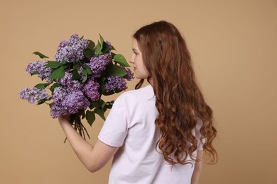 Photo of Teenage girl with bouquet of lilac flowers on beige background