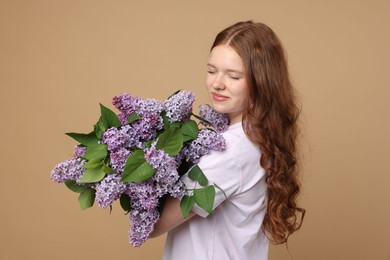 Photo of Beautiful teenage girl with bouquet of lilac flowers on beige background