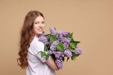 Photo of Smiling teenage girl with bouquet of lilac flowers on beige background. Space for text