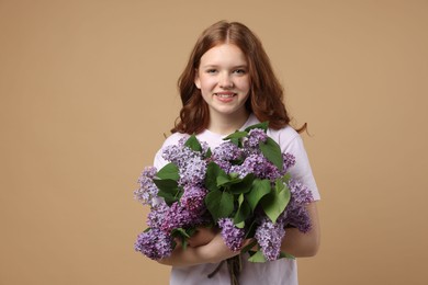 Photo of Smiling teenage girl with bouquet of lilac flowers on beige background