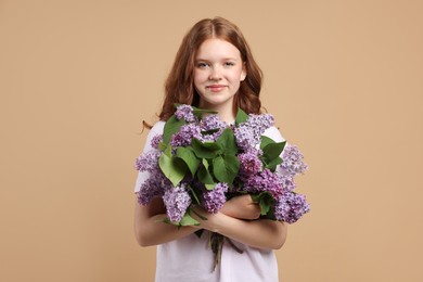 Photo of Beautiful teenage girl with bouquet of lilac flowers on beige background