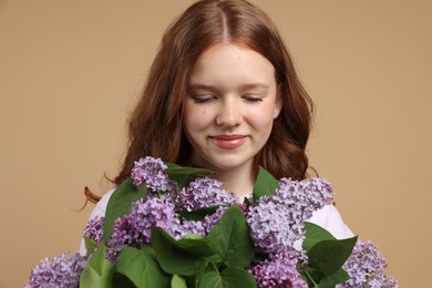 Photo of Beautiful teenage girl with bouquet of lilac flowers on beige background