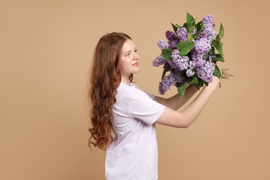 Photo of Beautiful teenage girl with bouquet of lilac flowers on beige background