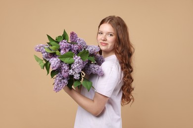 Photo of Beautiful teenage girl with bouquet of lilac flowers on beige background